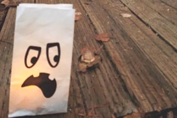 一个从里面点燃的白色纸袋，上面有一张幽灵的脸. 它坐落在一条木板路上.
